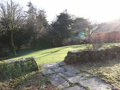 A stone pathway leading to a grassy lawn with trees and a low stone wall in a garden at Robin Cottage in Troutbeck