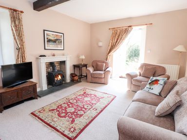 A living room with a TV on wooden stand a fireplace two armchairs a sofa and a red patterned rug at Robin Cottage in Troutbeck