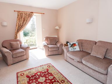 A living room with two armchairs and a sofa with cushions and a red patterned rug at Robin Cottage in Troutbeck