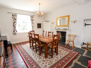 A dining room with a wooden table and chairs chandelier fireplace and a piano at Robin Cottage in Troutbeck