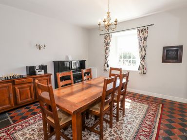A dining room with a wooden table and chairs a piano and a sideboard with a chess set at Robin Cottage in Troutbeck