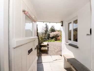 A white wooden door partially open showing a covered porch with built in bench and garden view at Robin Cottage in Troutbeck