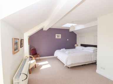 A bedroom with a double bed bedside table chairs paintings on the walls and a skylight at Robin Cottage in Troutbeck