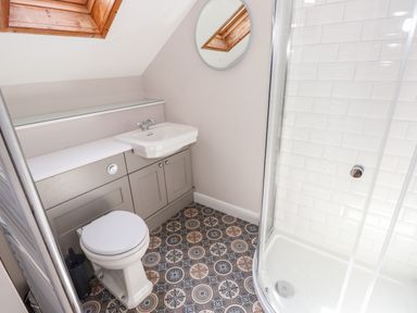 A bathroom with a toilet sink shower and a round mirror at Robin Cottage in Troutbeck
