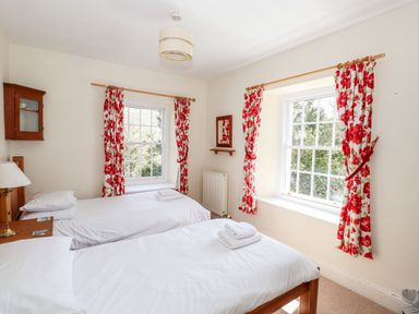 A bedroom with two single beds white linens floral curtains and two windows at Robin Cottage in Troutbeck