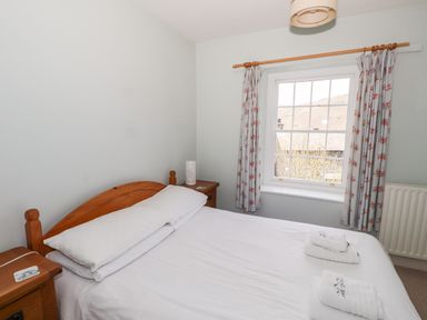 A bedroom with a double bed white sheets wooden bedside tables and a window with floral curtains at Robin Cottage in Troutbeck
