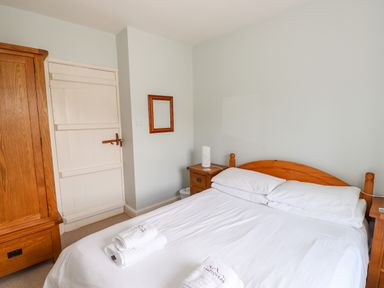 A bedroom with a wooden bed frame white bed linens bedside tables a wooden wardrobe and a white door at Robin Cottage in Troutbeck