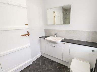 A bathroom with a white sink and cabinets under a mirror and a black countertop at Robin Cottage in Troutbeck
