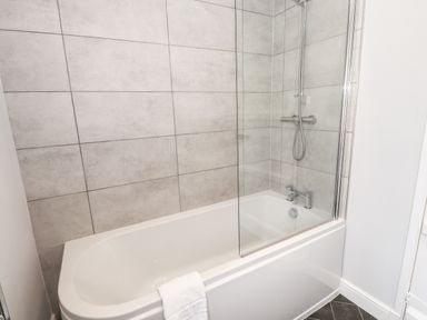 A bathroom with a bathtub shower and towel at Robin Cottage in Troutbeck