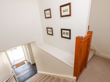 A carpeted staircase with wooden railing and framed pictures on the white wall at Robin Cottage in Troutbeck