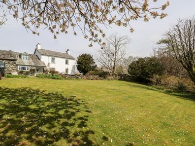 A grassy garden with scattered flower petals and a white cottage with stone walls in the background at Robin Cottage in Troutbeck