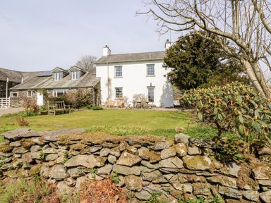 A white house with a grass lawn a wooden bench and outdoor seating behind a stone wall at Robin Cottage in Troutbeck