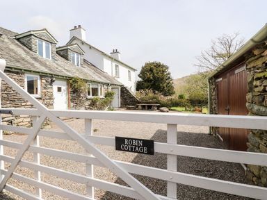 A white wooden gate with Robin Cottage sign in front of a stone cottage and courtyard at Robin Cottage in Troutbeck