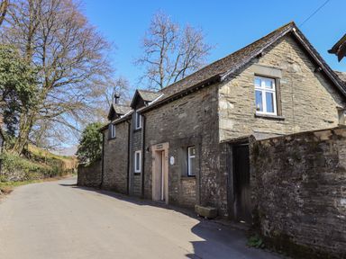 A stone house with white window frames beside a narrow road with trees in Troutbeck