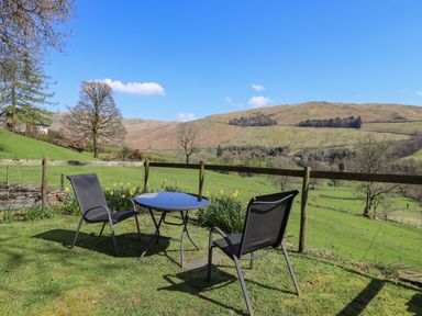 A garden area with two chairs and a round table overlooking green fields and hills at Boxwood Cottage in Troutbeck