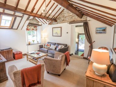 A living room with exposed wooden beams a leather sofa armchairs and a glass coffee table at Stablemans Cottage at Stepping Stones in Ambleside