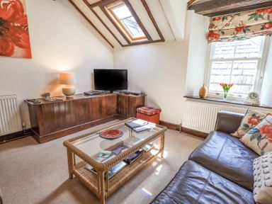 A living room with a leather sofa glass coffee table tv and window with floral curtains at Stablemans Cottage at Stepping Stones in Ambleside