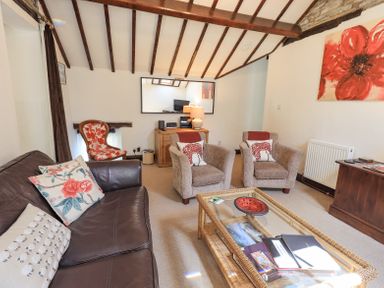 A living room with a leather sofa two armchairs a glass coffee table and a wooden cabinet at Stablemans Cottage at Stepping Stones Ambleside