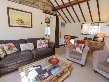 A living room with a brown leather sofa and two beige armchairs a glass coffee table and a wooden sideboard with a lamp at Stablemans Cottage at Stepping Stones Ambleside