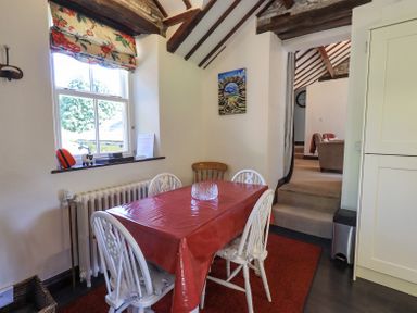 A dining area with a table covered by a red tablecloth and four chairs next to a window with floral blinds at Stablemans Cottage at Stepping Stones Ambleside