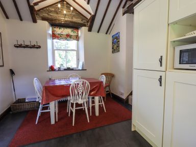 A dining area with a table covered by a red tablecloth and white chairs under a beamed ceiling at Stablemans Cottage at Stepping Stones in Ambleside