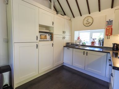 A kitchen with white cabinets a microwave a sink and a wall clock at Stablemans Cottage at Stepping Stones in Ambleside