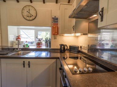 A kitchen with a sink, stove, kettle, toaster, utensils, and a clock above a window at Stablemans Cottage at Stepping Stones in Ambleside