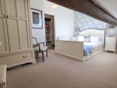 A bedroom with a bed bedside tables lamps a chair wardrobe and a floral wallpaper at Stablemans Cottage at Stepping Stones Ambleside
