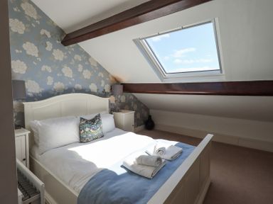 A bedroom with a white bed blue blanket pillows bedside tables lamps and a skylight window at Stablemans Cottage at Stepping Stones in Ambleside