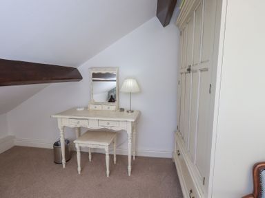 A small room with a dressing table, stool, table lamp, mirror, wardrobe, and a wooden beam at Stablemans Cottage at Stepping Stones in Ambleside