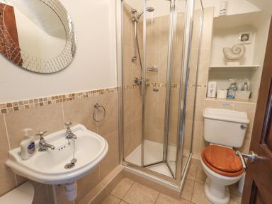 A bathroom with a shower enclosure a toilet with a wooden seat a white sink and a round mirror at Stablemans Cottage at Stepping Stones Ambleside