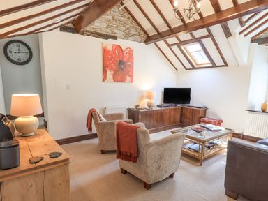 A living room with two armchairs a corner TV unit a coffee table and exposed wooden beams at Stablemans Cottage at Stepping Stones in Ambleside