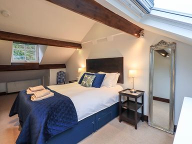 A bedroom with a bed blue bedding two bedside tables with lamps a large mirror and exposed wooden beams at Stablemans Cottage at Stepping Stones in Ambleside