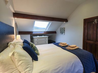 A bedroom with a bed pillows towels chest of drawers skylight and wooden door at Stablemans Cottage at Stepping Stones in Ambleside