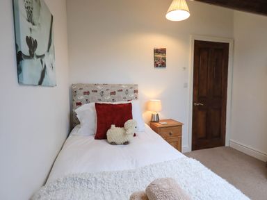 A bedroom with a single bed a wooden bedside table a lamp and a wooden door at Stablemans Cottage at Stepping Stones in Ambleside