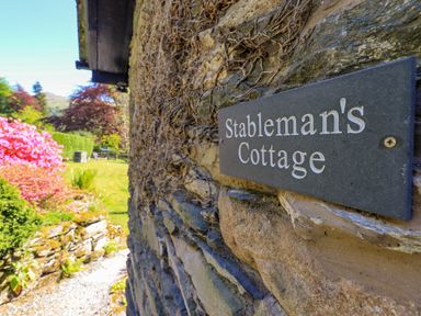 A stone wall with a Stablemans Cottage sign and a garden with plants and trees in the background at Stablemans Cottage at Stepping Stones in Ambleside