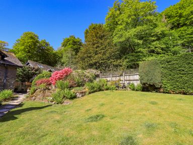 A garden with grass lawn plants flowers and trees next to stone buildings at Stablemans Cottage at Stepping Stones in Ambleside