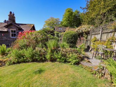 A garden with various plants and bushes and a small table with a chair at Stablemans Cottage at Stepping Stones in Ambleside