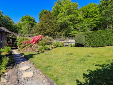 A garden with a grassy lawn flowers shrubs and a stone path at Stablemans Cottage at Stepping Stones in Ambleside