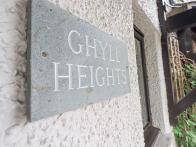 A close up of a sign that says Ghyll Heights on a rough white wall near a window and plants at Ghyll Heights in Ambleside