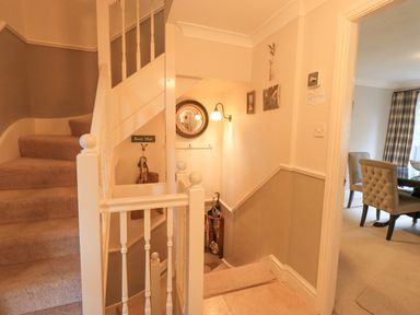 A stairway with beige carpet and white railing next to a hallway with hanging bags and umbrella at Ghyll Heights in Ambleside