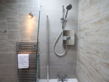 A shower area with a wall-mounted showerhead a glass partition and a towel rack with a white towel at Ghyll Heights in Ambleside