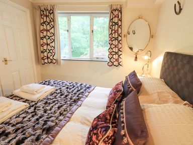 A bedroom with a bed pillows a bedside lamp a round wall mirror and patterned curtains at Ghyll Heights in Ambleside
