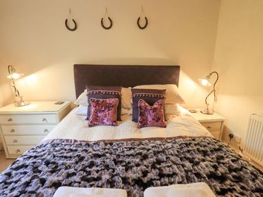 A bedroom with a bed with purple pillows and a textured blanket between two nightstands with lamps at Ghyll Heights in Ambleside