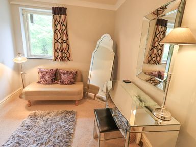 A room with a small beige sofa with two purple pillows a standing mirror and a glass desk with a chair and lamp at Ghyll Heights in Ambleside