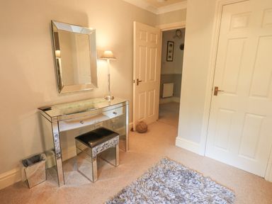 A room with a mirrored dressing table and stool a lamp a wall mirror and doors at Ghyll Heights Ambleside