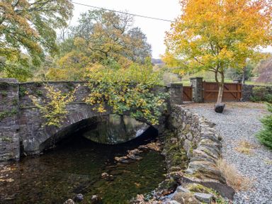 A bridge over a stream with a gate and trees at Goody Raise in Grasmere