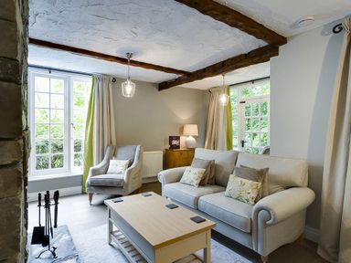A living room with a sofa a chair a coffee table and large windows at Acorn Cottage in Grasmere