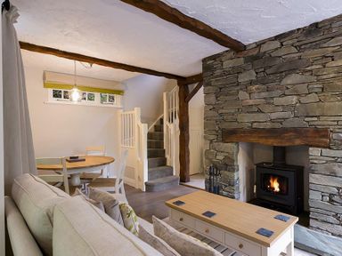 A living room with a stone fireplace a wooden coffee table a beige sofa a dining table and chairs and stairs at Acorn Cottage in Grasmere