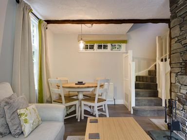 A dining area with a wooden round table and four chairs next to carpeted stairs and a stone fireplace at Acorn Cottage in Grasmere